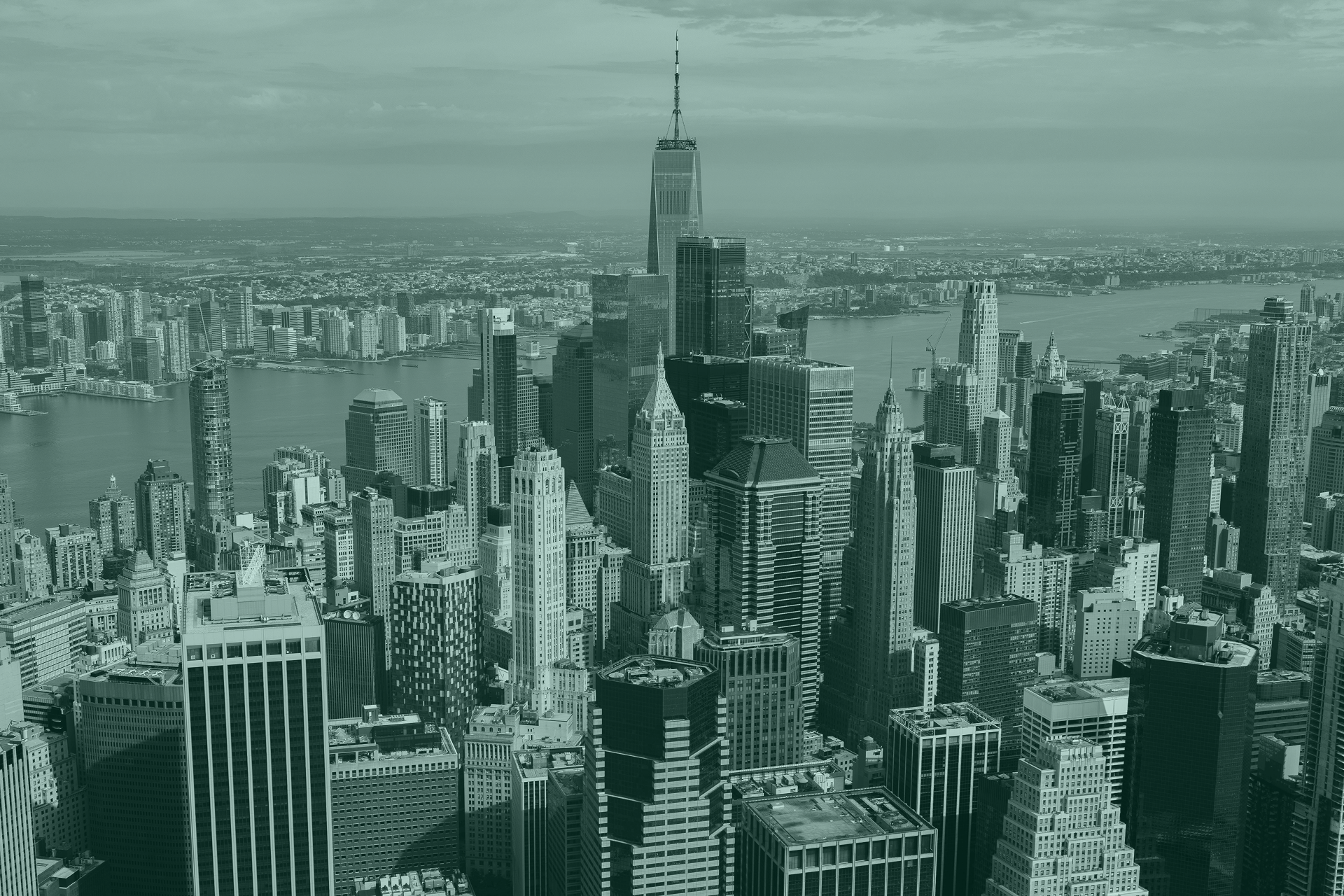 Aerial view of Manhattan with One World Trade Center towering at the center, under a pale sky.